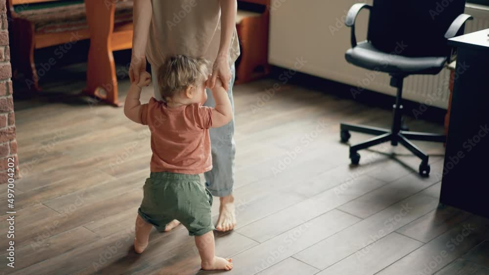 Little feet walking on floor, close-up. Baby learning to walk at home. Baby first steps. Smiling caring mother and cute little infant child girl cuddling in bedroom. Mum and child tender moments. Little feet walking on floor, close-up. Baby learning to walk at home. Baby first steps. Smiling caring mother and cute little infant child girl cuddling in bedroom. Mum and child tender moments.