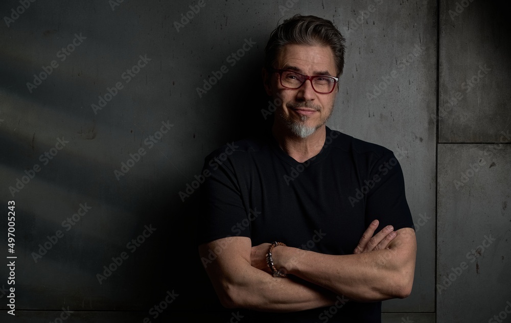 Portrait of happy casual middle aged, mid adult caucasian man in his 50s, smiling, standing against dark gray wall. . Copy space .