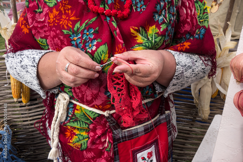  Close-up of the hands of a craftswoman in a folk Ukrainian costume with a hook in her hand