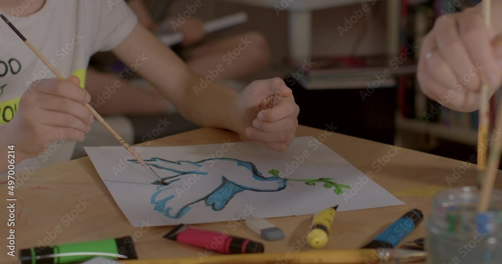 The brush makes a line. The hands of a teenager and a teacher draw a poster of a dove of peace. Preparing for a support action against the war. Use of water colors. The brush makes a line. The hands of a teenager and a teacher draw a poster of a dove of peace. Preparing for a support action against the war. Use of water colors.