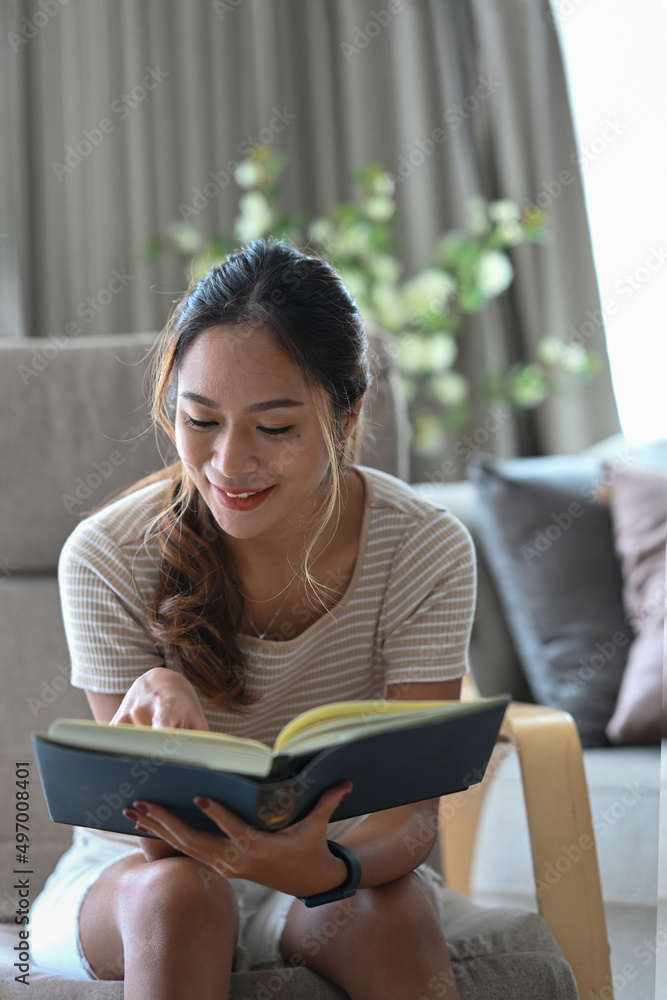 Peaceful young asian woman reading book while resting on comfortable armchair at home. Peaceful young asian woman reading book while resting on comfortable armchair at home.