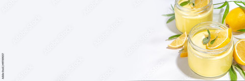 Lemon panna cotta dessert with fresh lemon wedges and sage leaves. Yellow citrus fruit panna cotta in portion jars on a white background Lemon panna cotta dessert with fresh lemon wedges and sage leaves. Yellow citrus fruit panna cotta in portion jars on a white background