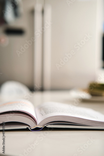 Open hardcover book with white pages lies on artificial stone table at kitchen, fridge on background. Books spine. Selective focus. Vertical stories background.