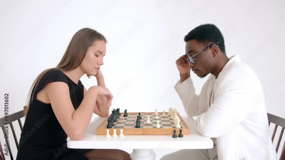 Caucasian girl and an african american guy are playing chess in studio. The concept of racial confrontation. Slow motion