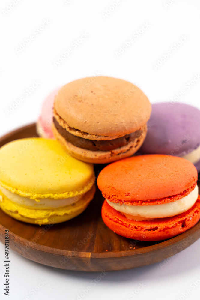 Multicolored macarons on a wooden plate on a white background. Multicolored macarons on a wooden plate on a white background.