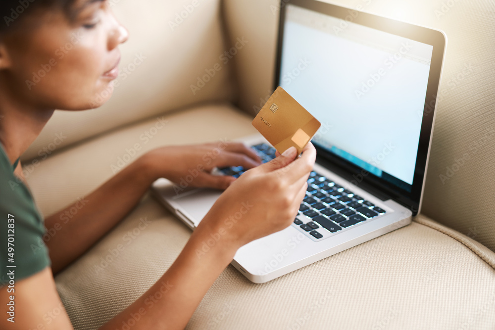 Internet banking on the sofa. Cropped shot of a woman using her laptop on the sofa at home while holding a bankcard. Internet banking on the sofa. Cropped shot of a woman using her laptop on the sofa at home while holding a bankcard.