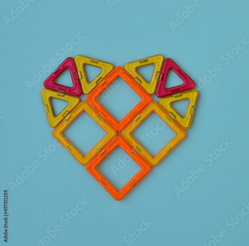 Heart-shaped, lined with multicolored parts of a magnetic constructor on blue background. photo