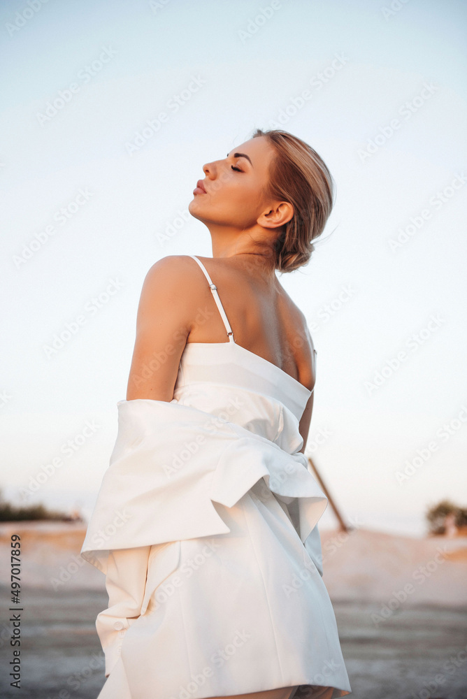 Gorgeous lady in stylish white suit standing on sand Gorgeous lady in stylish white suit standing on sand