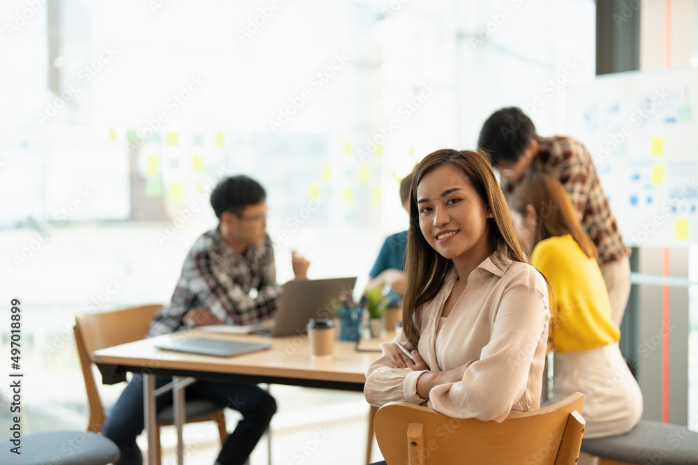 Attractive young Asian business woman smiling and looking over shoulders at business meeting with co-workers Attractive young Asian business woman smiling and looking over shoulders at business meeting with co-workers