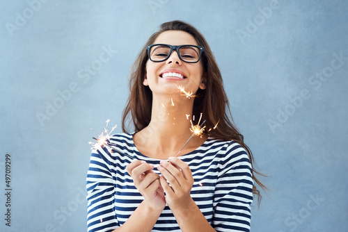 Everyday Im sparklin. Studio portrait of a beautiful young woman holding sparklers against a blue background. photo