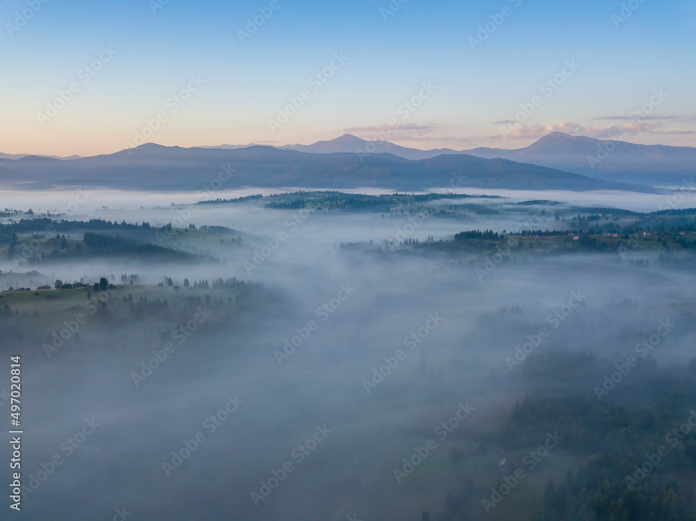 Flight over fog in Ukrainian Carpathians in summer. Mountains on the horizon. Aerial drone view.