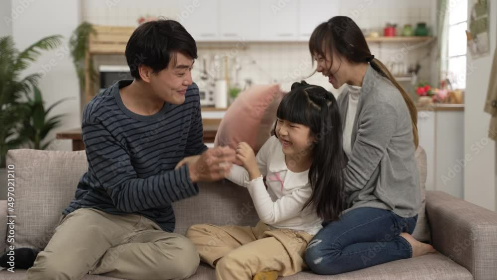 slow motion of happy Korean father, mother and daughter playing tickle on living room couch at home. the woman having fun hitting the man with cushion slow motion of happy Korean father, mother and daughter playing tickle on living room couch at home. the woman having fun hitting the man with cushion