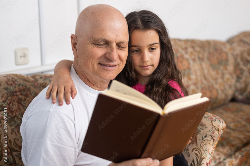 Happy grandfather and granddaughter reading book together at home. Close up. Happy grandfather and granddaughter reading book together at home. Close up.