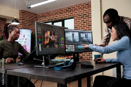 Valokuva Professional videographer sitting at desk while coworker helping her with film footage visual quality improvement