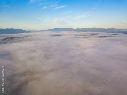 Flight over fog in Ukrainian Carpathians in summer. A thick layer of fog covers the mountains with a solid carpet. Mountains on the horizon. Aerial drone view.