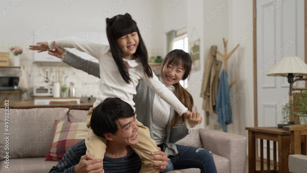 slow motion of excited Asian daughter playing and sitting on her dad’s shoulders in living room while her mom is holding her arms and having a good laugh slow motion of excited Asian daughter playing and sitting on her dad’s shoulders in living room while her mom is holding her arms and having a good laugh