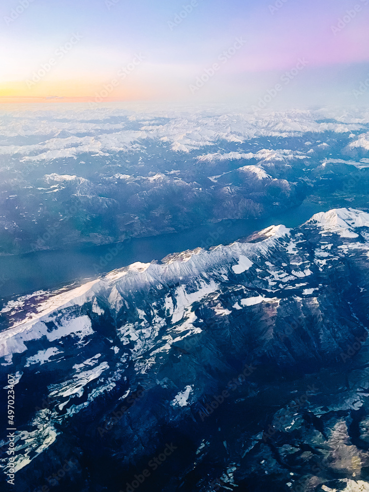 aerial view from airplane, view of mountains with snow-capped peaks on sunset