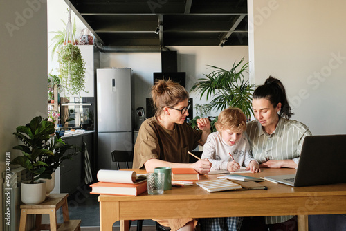 Child doing homework at table in kitchen together with homosexual mothers