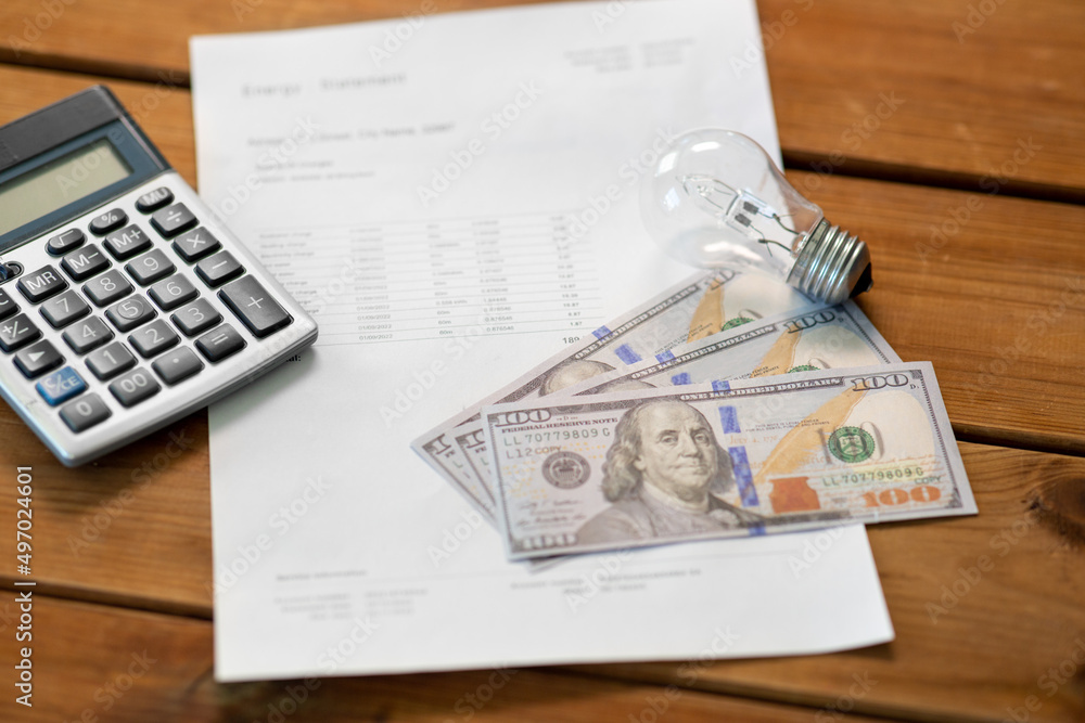 Obraz premium electricity, energy crisis and power consumption concept - close up of utility bill, calculator, money and lightbulb on wooden table