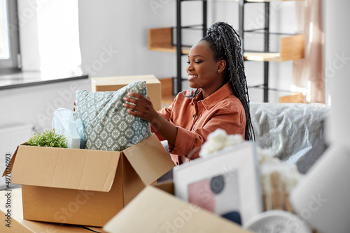 moving, people and real estate concept - happy smiling woman unpacking boxes sitting on sofa at new home photo