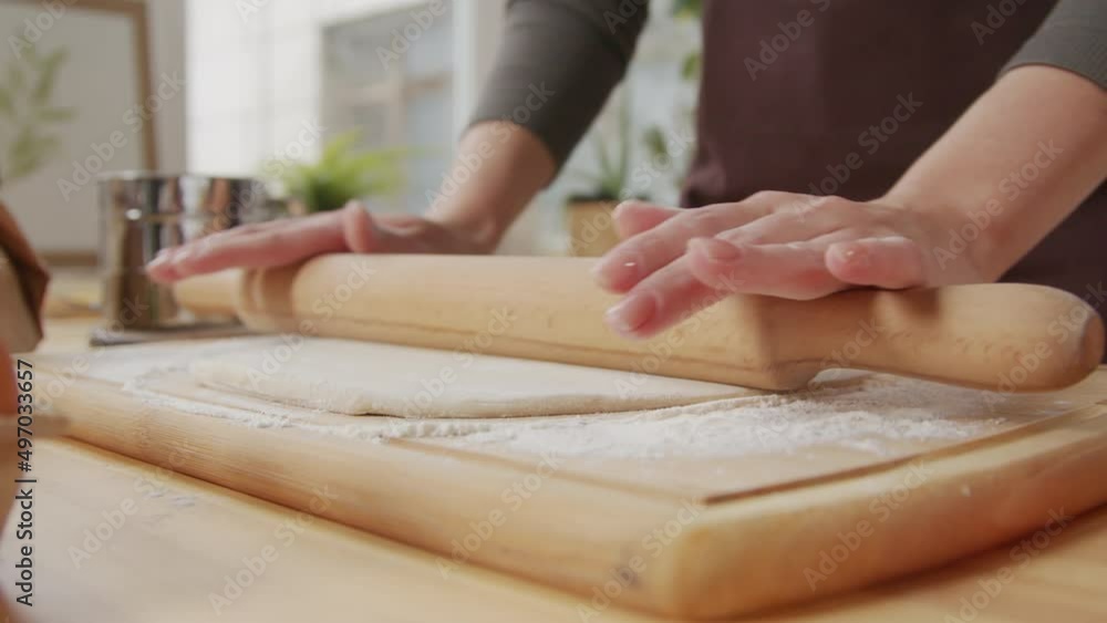 Close up shot of female hands rolling dough on wooden board at kitchen table Close up shot of female hands rolling dough on wooden board at kitchen table