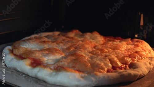 Close up view of cheese on pizza melts from oven heat. Delicious pizza richly strewn with cheese is cooked in the oven. Tasty Italian pizza cheese roasted in the oven on a stone. High quality 4k video