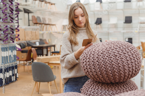 Young caucasian woman buyer choosing knitted pouf in furniture shop