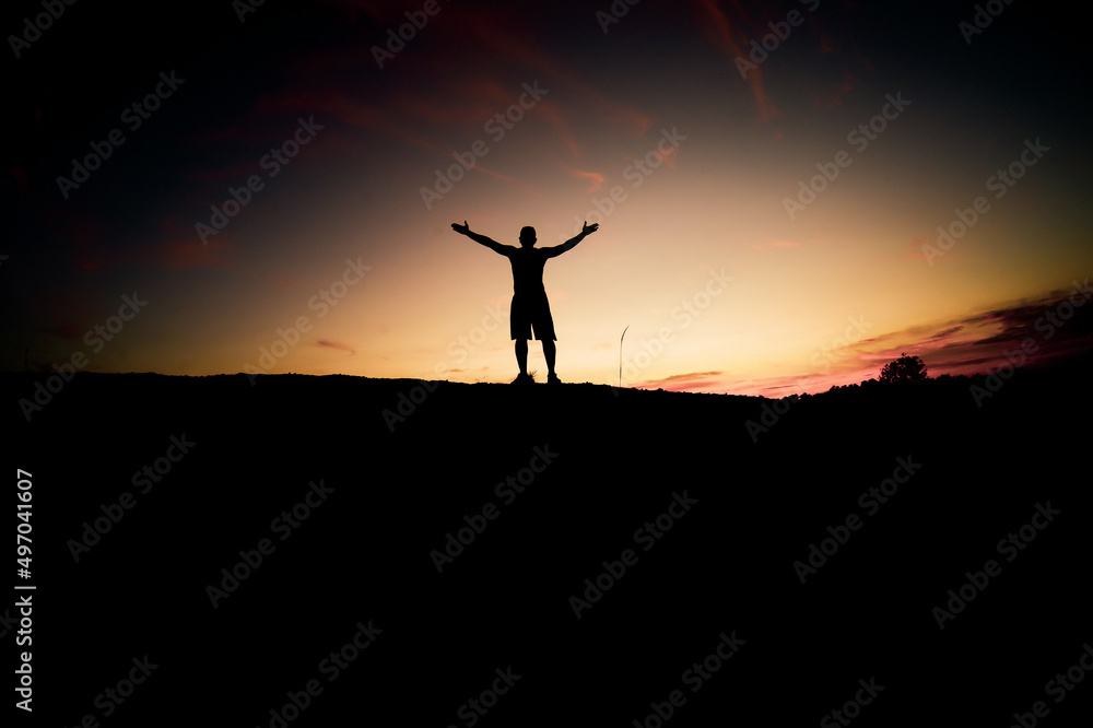 The silhouette of a man is standing with his hands up in happiness.