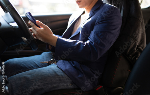 Man sitting in car using mobile phone to text while driving. Close-up of businessman while driving typing message on mobile phone. © Wasan