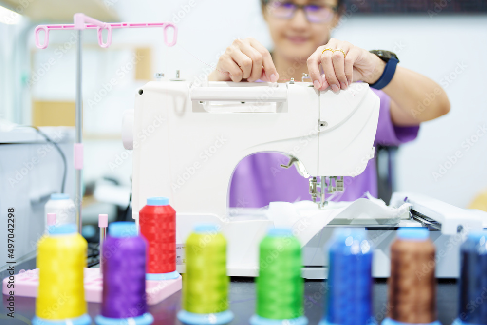 Embroidery, handicrafts, SME, family business Portrait of an Asian female designer picking up sewing threads for Design patterns using automatic embroidery machines according to customer orders.