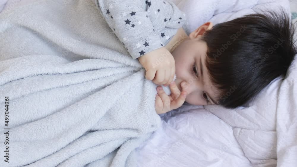 close up video with a 4 years old little kid, boy, sucking his big finger. child with a bad habbits that withstand in time. boy in pijama with stars print with grey soft blanket is on his bed for kids close up video with a 4 years old little kid, boy, sucking his big finger. child with a bad habbits that withstand in time. boy in pijama with stars print with grey soft blanket is on his bed for kids