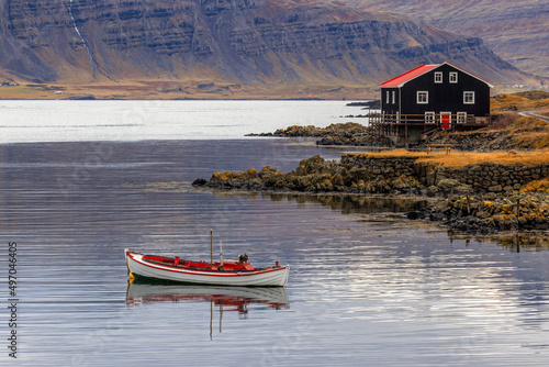 Small boat and black wooden house, Djupivogur, Eastfjords, Iceland. Landscape shot in autumn with mountain background. photo