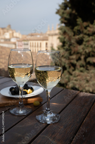 Two glasses of Spanish dry rueda white wine served with olives on roof terrace with view on old part of Andalusian town Granada, Spain