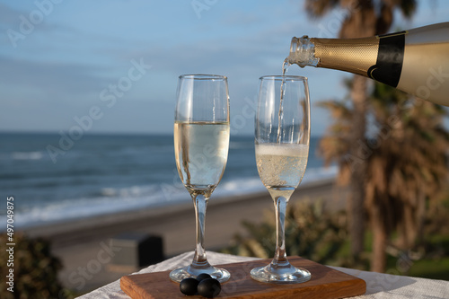 Pouring of Spanish cava sparkling wine is glasses with view on blue sea and sandy beach, Costa del Sol vacation destination, Andalusia, Spain