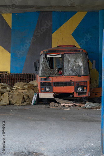 An old broken and rusting red bus stands in an abandoned parking lot