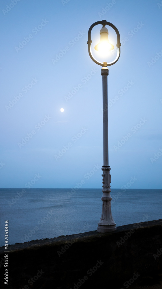 lamppost illuminated at dusk with the sea in the background