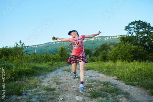 A school-age girl in pink clothes runs along a dirt road and jumps for joy.