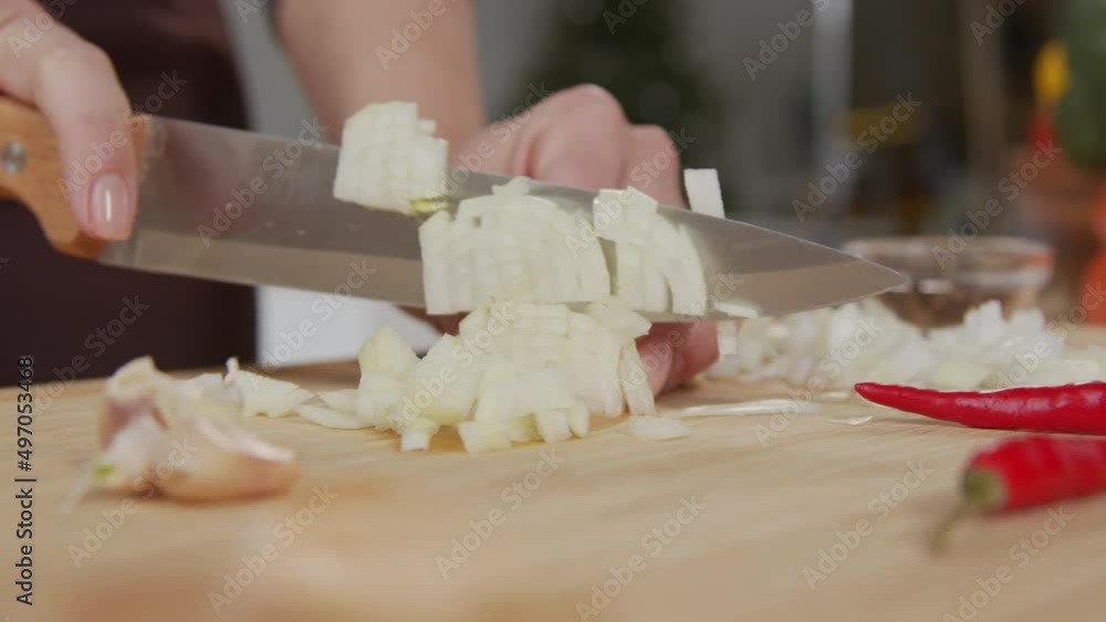 Close up shot of female hands chopping fresh onion with knife on wooden cutting board Close up shot of female hands chopping fresh onion with knife on wooden cutting board