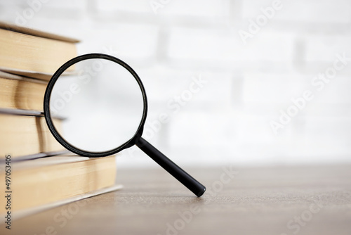 education and research concept - stack of books and magnifying glass on the table in library, copy space over white background