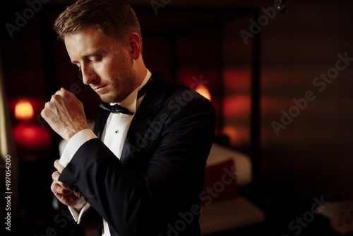 A close-up of a cropped frame of a man groom in an expensive classic costume,and white shirt getting ready for event. The future husband is in a hurry and dressing up for wedding celebration. photo