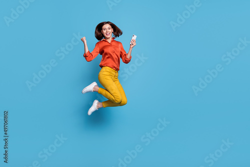 Full length body size view of attractive cheery lucky trendy girl jumping using device rejoice isolated over bright blue color background