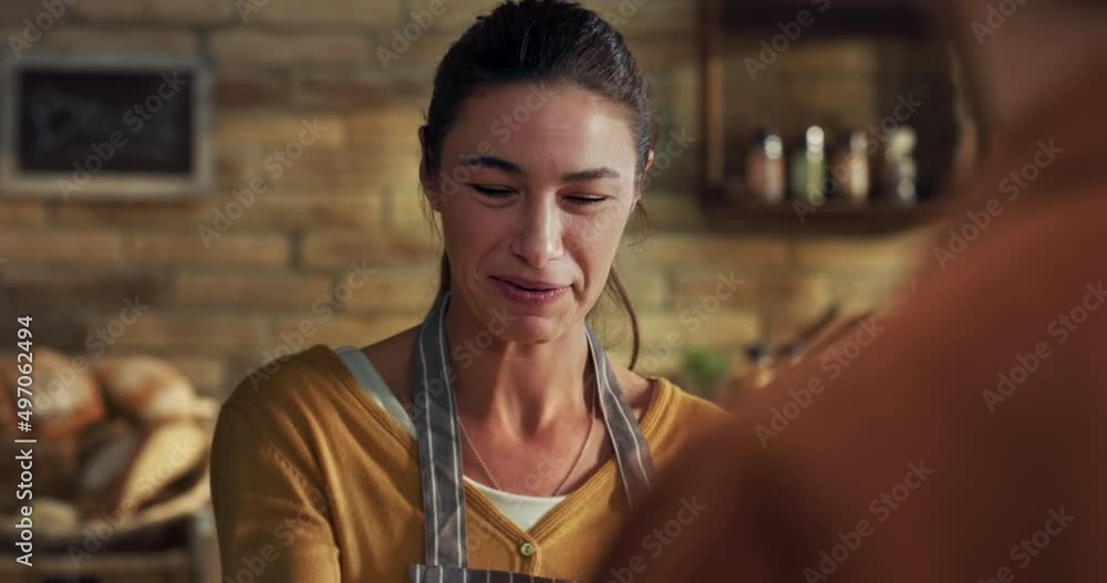 Cinematic shot of young friendly saleswoman passing fresh bread over counter to customer paying with smartphone using NFC technology in bakery shop.