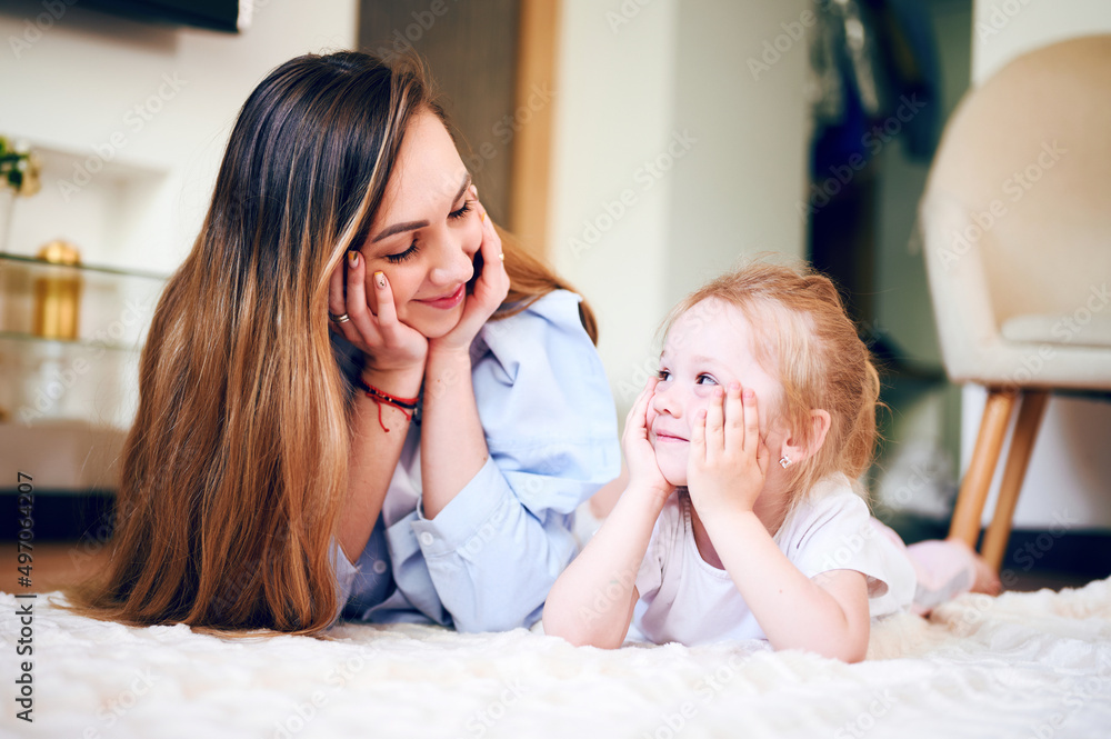 Young happy mother with her preschool daughter lie on the floor laughing and having a good time together Young happy mother with her preschool daughter lie on the floor laughing and having a good time together