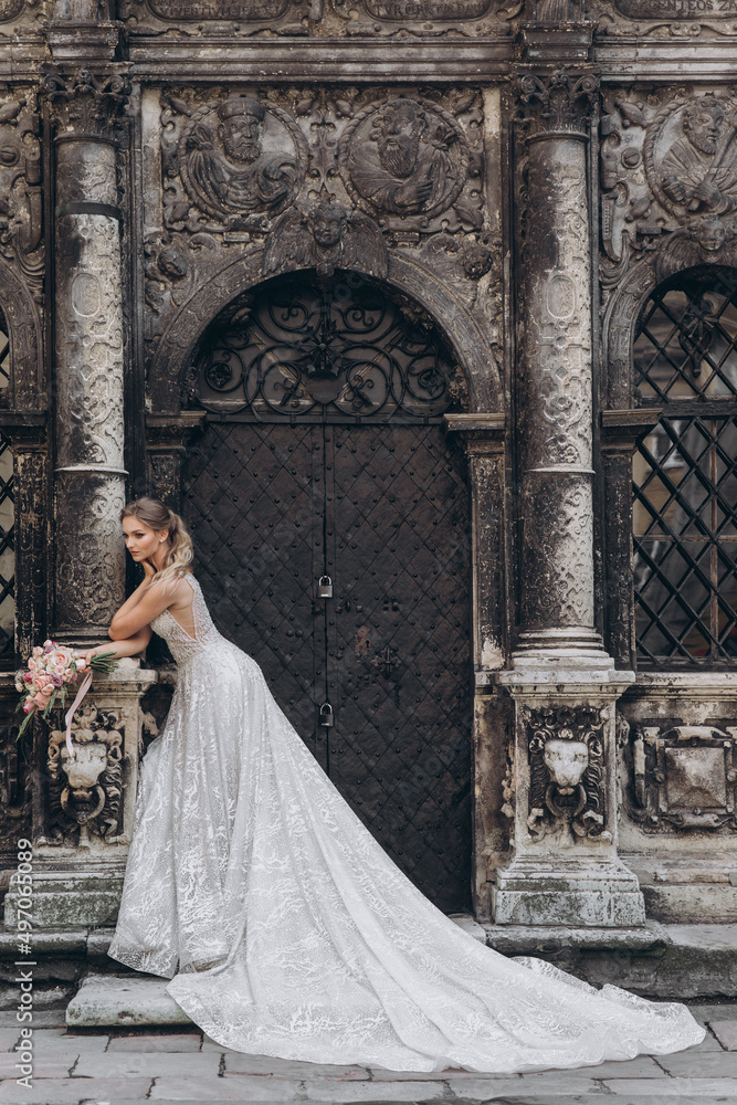 Fototapeta premium Beautiful bride in a long white wedding dress on a background of black old building
