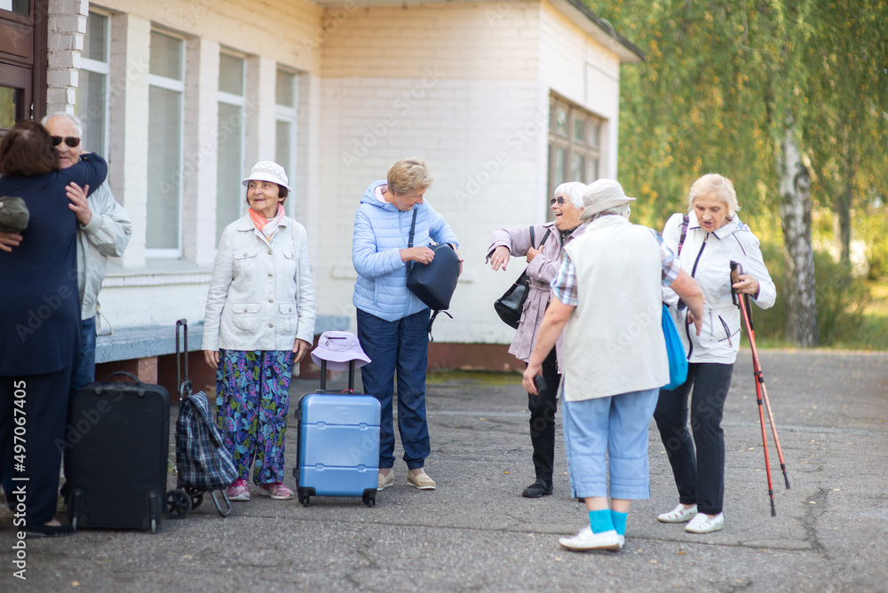 A group of elderly friends with suitcases and bags gather at the train station to go on a trip