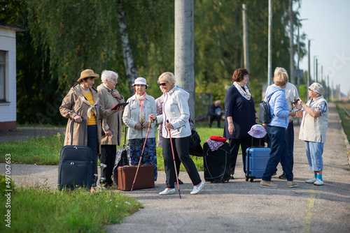 Group of active cheerful seniors with suitcases standing on peron