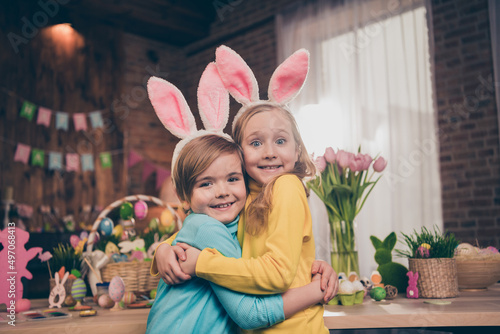 Portrait of two idyllic adorable kids cuddle toothy smile look camera wear rabbit ears headband house indoors