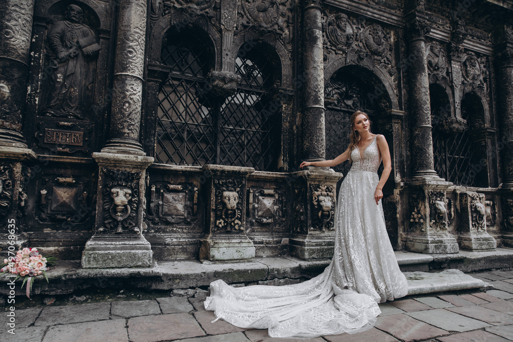 Charming bride in a long white wedding dress on a background of black old building