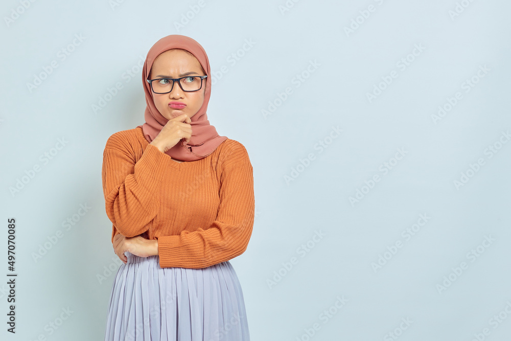 Naklejka premium Pensive young Asian Muslim woman in brown sweater and glasses, holding chin while thinking something isolated on white background. people religious lifestyle concept