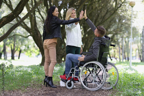 Joyful two woman and a man in wheelchair join hands.